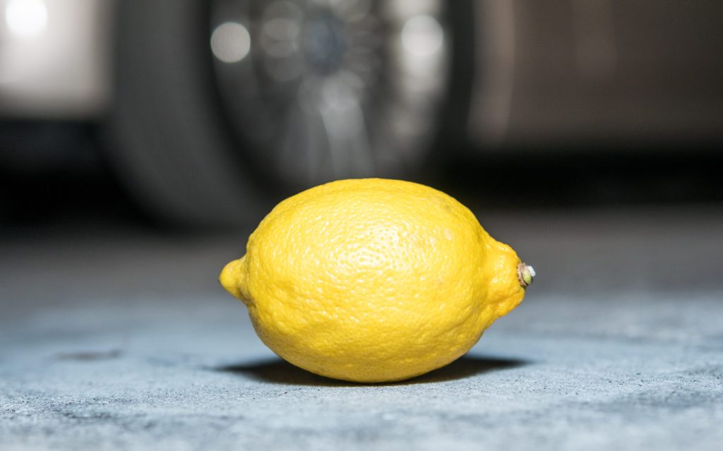 A lemon on the floor. A car is blurred in the background.